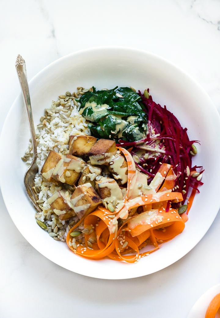 Glory bowl salad with brown rice, crispy tofu, carrots, beets, wilted spinach, toasted seeds and a delicious tahini dressing. Vegan and gluten free.