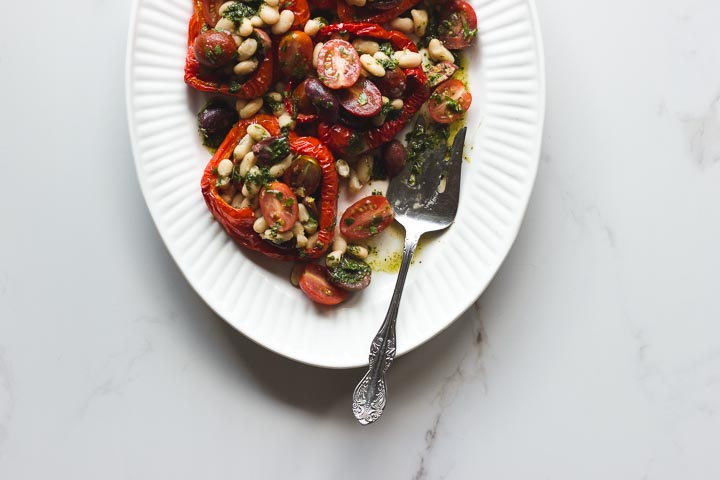 Stuffed roasted red peppers with cherry tomatoes, white beans and olives. Covered in a basil dressing. Vegan and gluten free.
