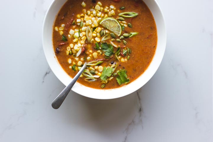 Vegan roasted tomato soup with black beans and polenta. Topped with sweet corn salsa, cilantro, lime and toasted pumpkin seeds.